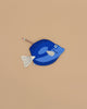 A Surgeon Fish Pencil Case, crafted from blue cotton with a white tail and fins, rests on a beige surface. A pencil peeks out from its zippered opening.