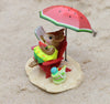 The Wee Forest Folk Tiny Collectible - Perfect Beach Day! features a rabbit in a yellow dress on a red chair under a watermelon umbrella, holding watermelon with a green bag on sand—capturing the charming beach scene.