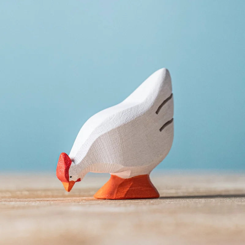 The Bumbu Handmade Wooden White Hen is a small, eco-friendly figurine crafted from sustainable Romanian wood, featuring a white body, orange beak and feet, and a red comb. It stands on a light surface against a blue background.