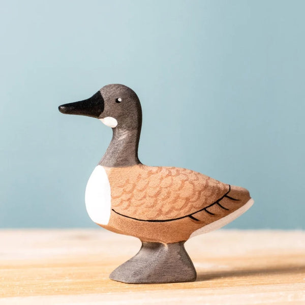 The Bumbu Handmade Wooden Wild Goose, featuring painted brown and white details, stands on a light wooden surface with a soft blue background, highlighting the charm of this eco-friendly children's toy.