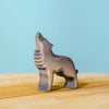 The Bumbu Handmade Wooden Wolf Howling figurine, small and handcrafted, stands on a light wooden surface against a blue background.