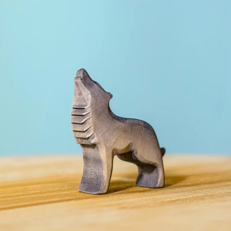 The Bumbu Handmade Wooden Wolf Howling figurine, small and handcrafted, stands on a light wooden surface against a blue background.