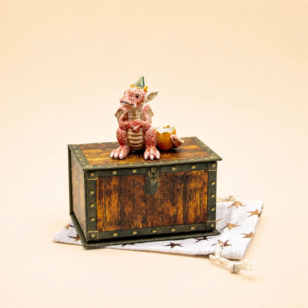 Sure! Here is a rewritten version of the sentence using the provided product data: The Dragon Cake Topper - Final Sale, a small red handcrafted collectible figurine, is displayed sitting on a keepsake treasure chest. Beneath the chest rests a white bag adorned with star designs, all arranged against a plain beige background.