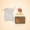 A small gray star-patterned pouch, a yellow pencil, a wooden keepsake treasure chest with “Camp Hollow” on the lid, and a red Dragon Cake Topper - Final Sale are arranged on a cream background.