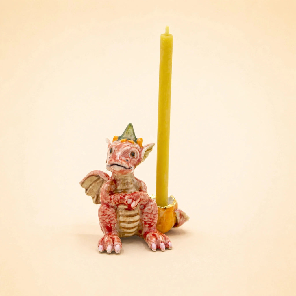 A small red Dragon Cake Topper with a yellow crown holds a yellow candle upright on a beige background, making it an enchanting handcrafted collectible perfect for any fantasy lover.