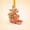 A small handcrafted collectible ceramic “Dragon Cake Topper - Final Sale” figurine with red and gold scales holds a candle on its back, sitting upright with a friendly expression against a plain background.