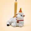 A charming handcrafted porcelain figurine, the Goat Cake Topper features a small white goat wearing a red and yellow party hat and a red collar, holding a beige candle on its back—an adorable cake topper that doubles as a unique birthday decoration.