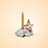 A small porcelain goat figurine, perfect as a cake topper, wears a red and yellow party hat and has a red collar with a bell. The goat holds a lit beige candle on its back and is photographed against a plain, light background. Product Name: Goat Cake Topper - Final Sale.