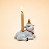 A handcrafted Goat Cake Topper, featuring a white goat figurine sporting a red and yellow party hat and carrying a lit beige candle on its back, makes an adorable birthday decoration against a plain light background.