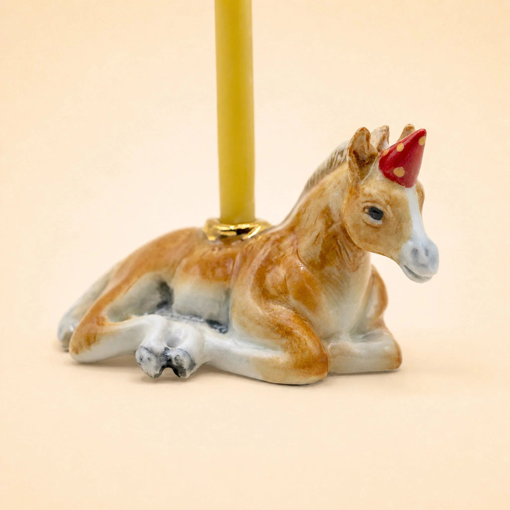 A charming keepsake, the Horse Cake Topper features a handcrafted design resembling a resting horse with gold accents, set against a light beige background.