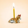 A yellow candle is placed on the Horse Cake Topper—a ceramic horse figurine featuring subtle gold accents and a small red party hat—set against a plain beige background.