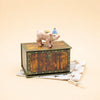 A charming Pig Cake Topper featuring a small pig figurine with a party hat and a coin on its back stands atop a wooden chest, set on a star-patterned cloth against a beige background—an ideal keepsake birthday decoration and handcrafted collectible.