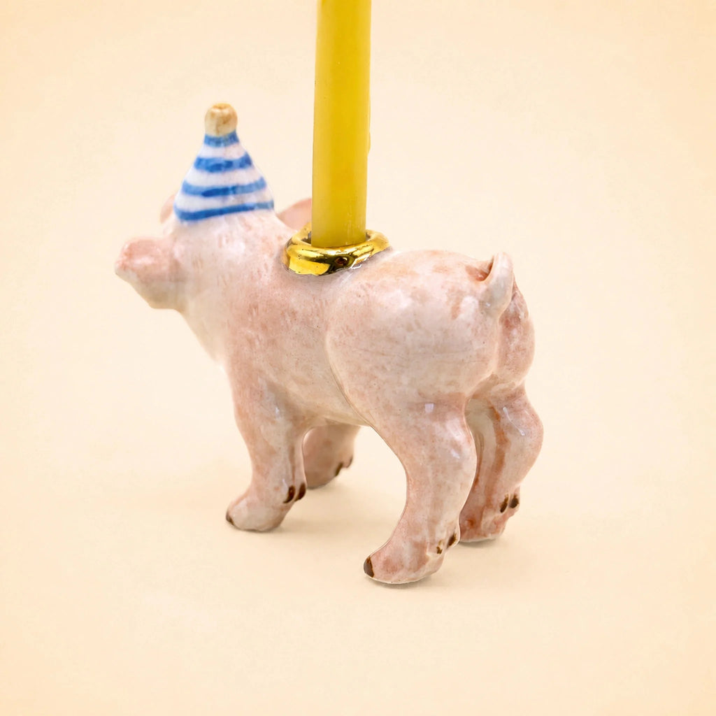Pig Cake Topper - Final Sale: A charming ceramic pig figurine wearing a blue-striped party hat and carrying a yellow candle on its back, set against a plain beige background—a delightful handcrafted collectible and whimsical keepsake birthday decoration.