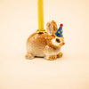 The Bunny Rabbit Cake Topper - Final Sale features a handcrafted collectible ceramic bunny figurine wearing a blue party hat with yellow dots and carrying a yellow candle on its back, displayed against a plain, light background.