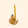 A hand-painted birthday decoration, the Mouse Cake Topper - Final Sale is a ceramic figurine featuring a mouse wearing a blue party hat and holding an upright lit yellow candle while sitting on its back feet against a plain light background.