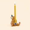Introducing the Mouse Cake Topper - Final Sale: a whimsical, hand-painted cake topper featuring a seated brown mouse wearing a blue party hat and holding an upright yellow candle between its legs. This charming birthday decoration adds festive flair to any celebration and serves as a delightful collectible keepsake.