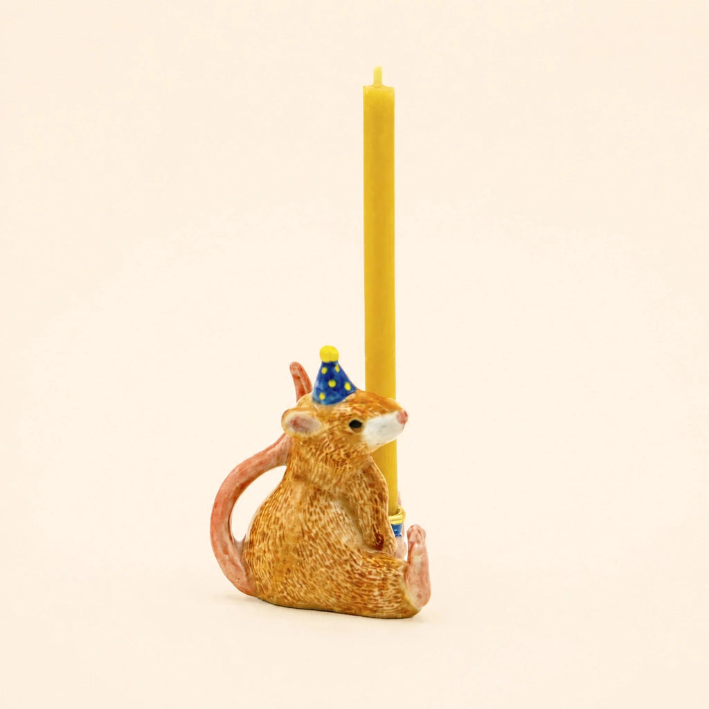 The Mouse Cake Topper – Final Sale features a hand-painted ceramic mouse in a blue party hat, sitting upright and holding a yellow candle against a simple light backdrop—an adorable birthday decoration perfect as a collectible keepsake.