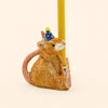 Certainly! Here’s a rewritten sentence using the product data: The Mouse Cake Topper – Final Sale is a hand-painted ceramic figurine featuring a mouse wearing a blue party hat with yellow dots, holding a yellow candle upright with its feet and tail, set against a plain light background.