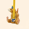 The Mouse Cake Topper - Final Sale features a ceramic mouse wearing a blue party hat and holding a yellow candle between its paws, making it an adorable hand-painted birthday decoration as well as a charming collectible keepsake.