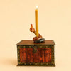 A yellow beeswax birthday candle stands upright, held by the Snake Cake Topper, which sits atop a wooden treasure chest with metal accents and a lock.