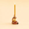 A yellow beeswax birthday candle stands upright in the hand-painted “Snake Cake Topper – Final Sale,” a ceramic candle holder shaped like a coiled snake wearing a small party hat, set against a plain beige background. This whimsical piece makes for a charming collectible.