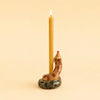 A brown, hand-painted collectible Snake Cake Topper with a red-tipped hood holds a lit, tall, yellow candle against a plain beige background.