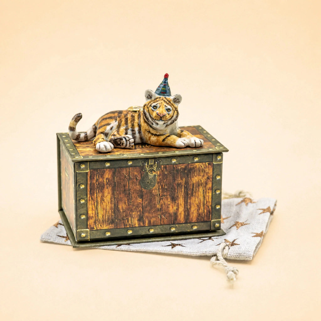 A “Tiger Cake Topper - Final Sale,” a small handcrafted collectible figurine of a tiger wearing a party hat, rests atop a decorative wooden keepsake treasure chest placed on a star-patterned cloth against a beige background.