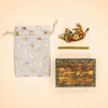 A “Tiger Cake Topper - Final Sale,” along with a gold star-patterned drawstring bag, a handcrafted collectible gold stick, and a small wooden “camp hollow” keepsake box resembling a treasure chest, are all arranged on a beige background.