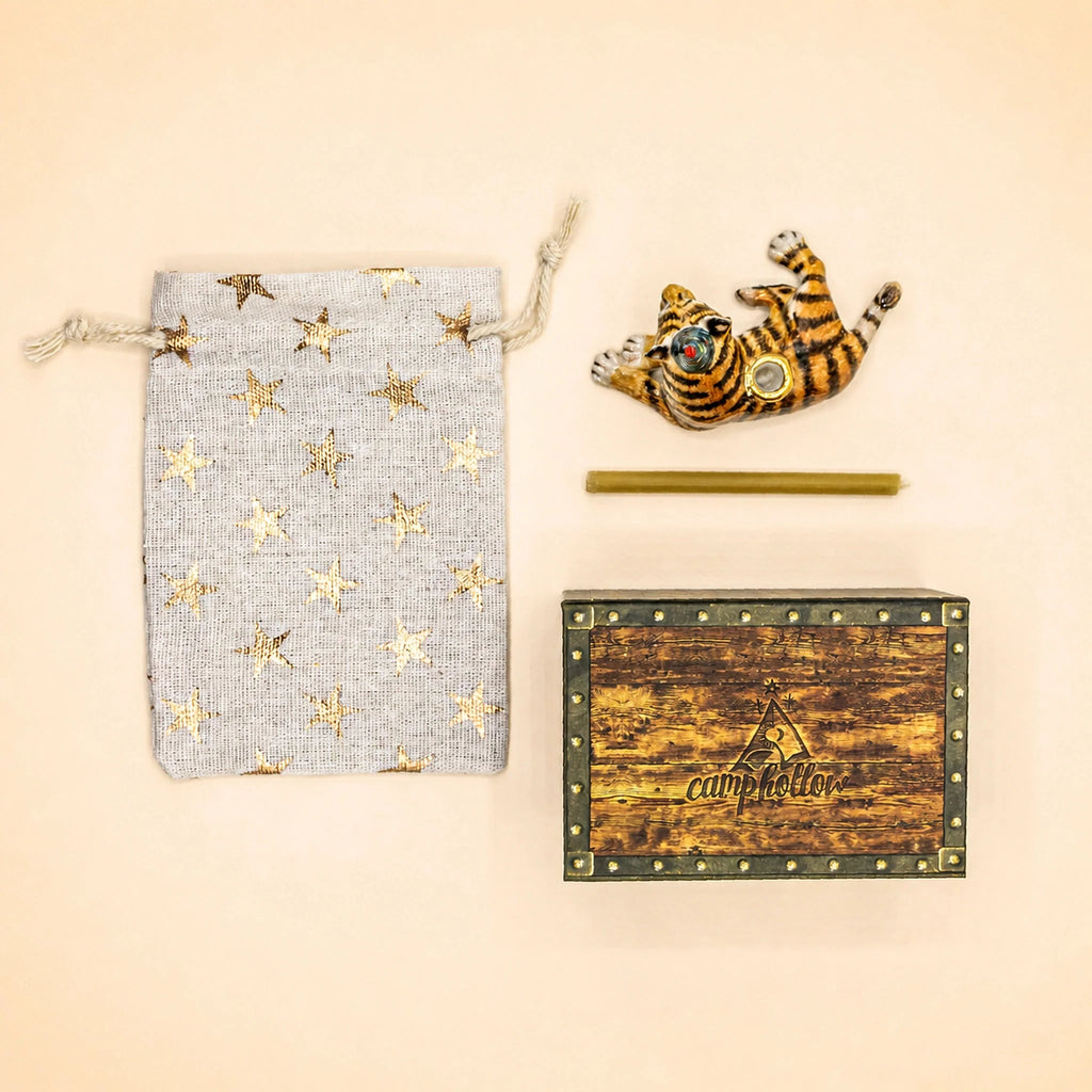 A “Tiger Cake Topper - Final Sale,” along with a gold star-patterned drawstring bag, a handcrafted collectible gold stick, and a small wooden “camp hollow” keepsake box resembling a treasure chest, are all arranged on a beige background.