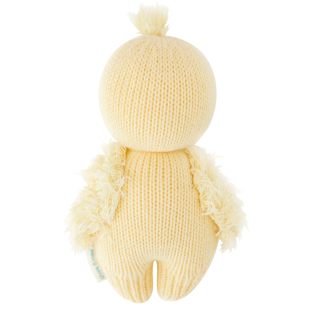A soft, yellow hand-knit Cuddle + Kind Baby Duckling with a round head and body, featuring fluffy wings at the sides, displayed against a white background.