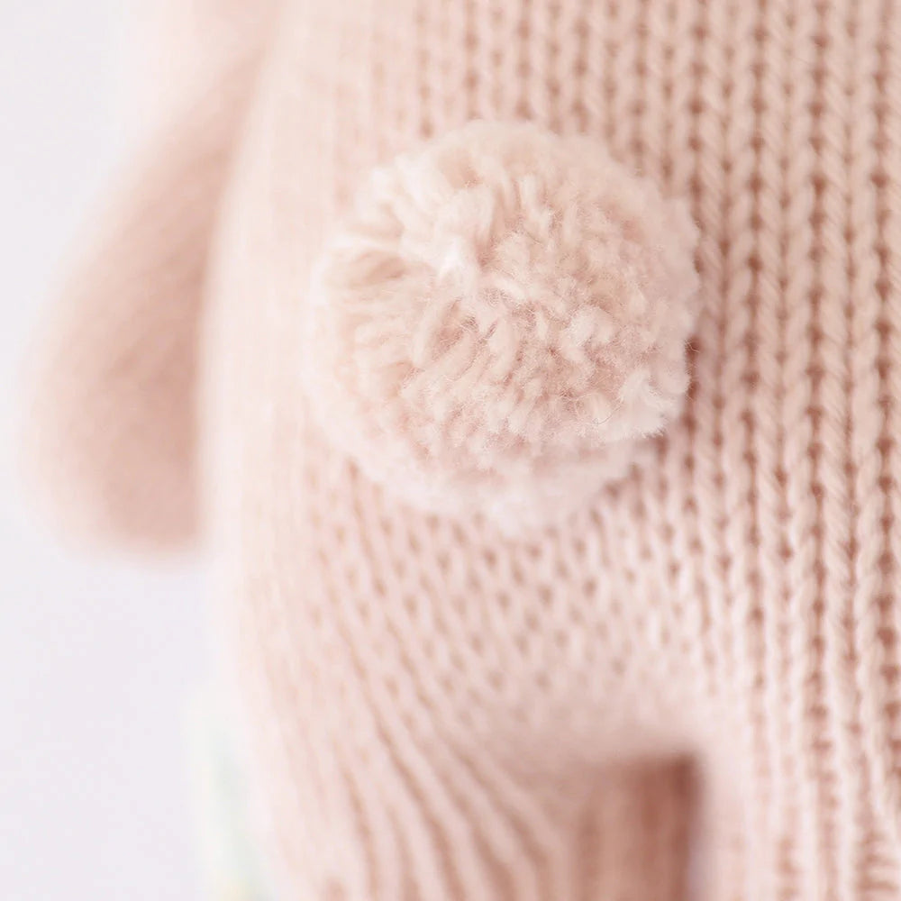 Close-up of a Cuddle + Kind Baby Bunny hand-knit fabric with a fluffy pom-pom attached, displaying a soft texture and detailed stitching.