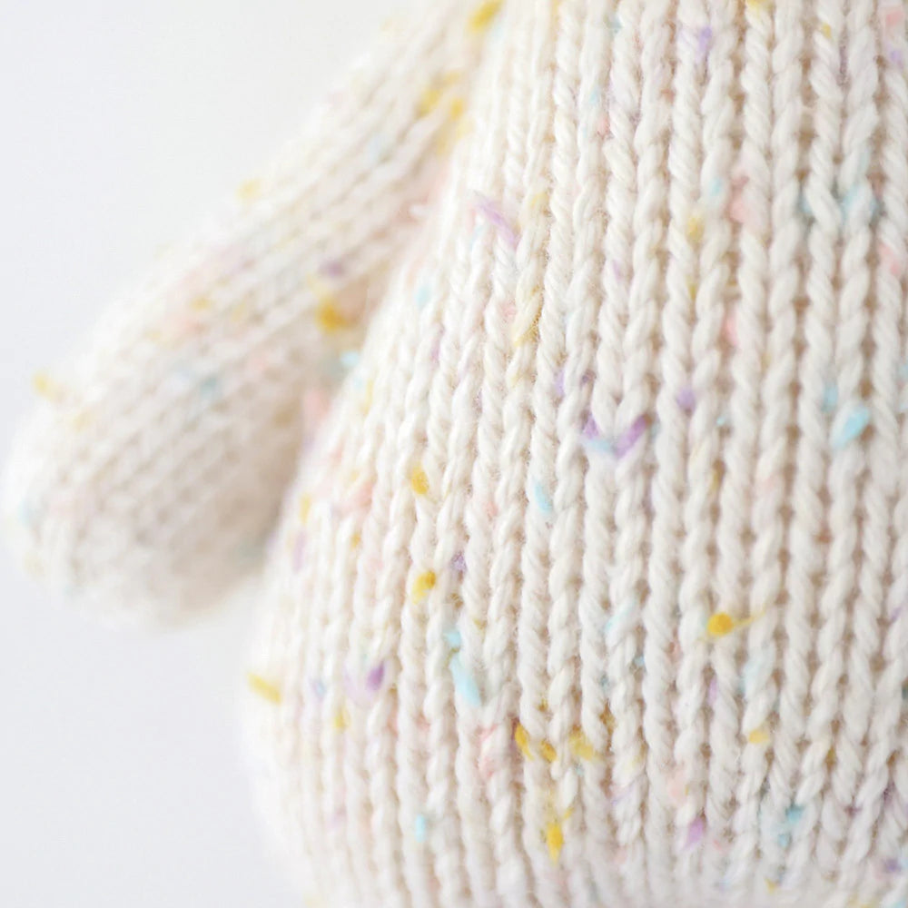 Close-up view of a soft, hand-knit fabric with delicate pastel flecks integrated into the creamy white Cuddle + Kind Baby Kitten yarn, emphasizing the texture and cozy appearance.