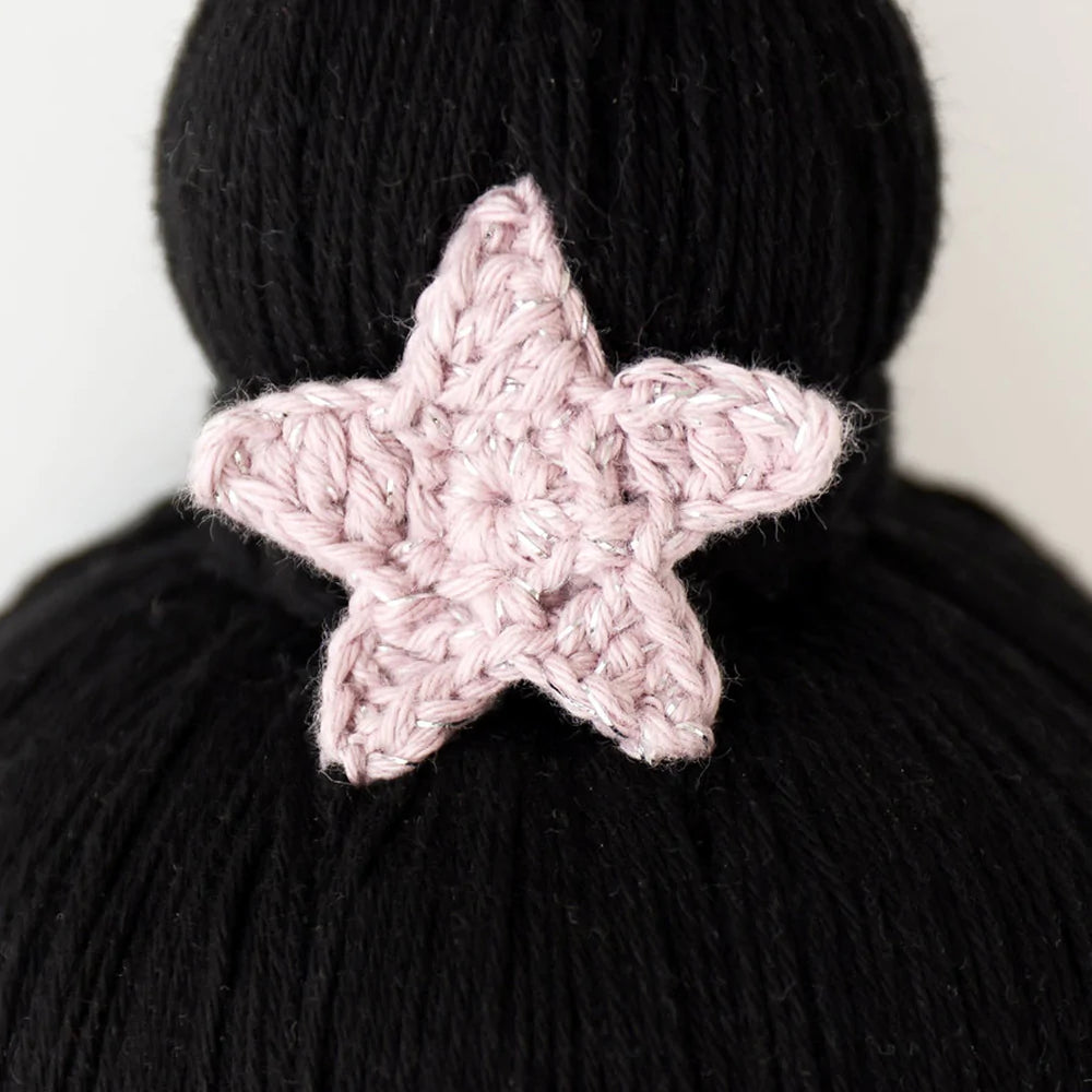 Close-up of a pink crocheted Cuddle + Kind Luna The Mermaid attached to a black hand-knit background, highlighting the detailed stitch work of the star.