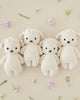 Four Cuddle + Kind Baby Lambs, hand-knit from Peruvian cotton yarn, with white bodies and cream faces, each adorned with pink floral crowns, arranged symmetrically on a beige background scattered with small.
