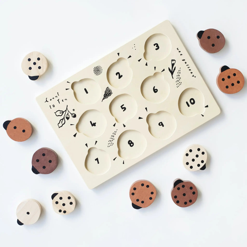 A Wooden Tray Puzzle - Count to 10 Ladybugs made from sustainably sourced rubberwood, featuring numbered holes from 1 to 10 and small wooden ladybug counters on a white background. Each hole includes a simple, engraved illustration.