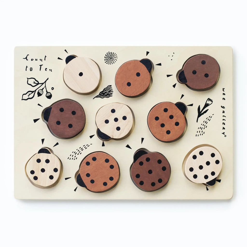Wooden Tray Puzzle - Count to 10 Ladybugs featuring round pieces with various dot patterns representing numbers, arranged on a board with decorative leaf and feather designs.