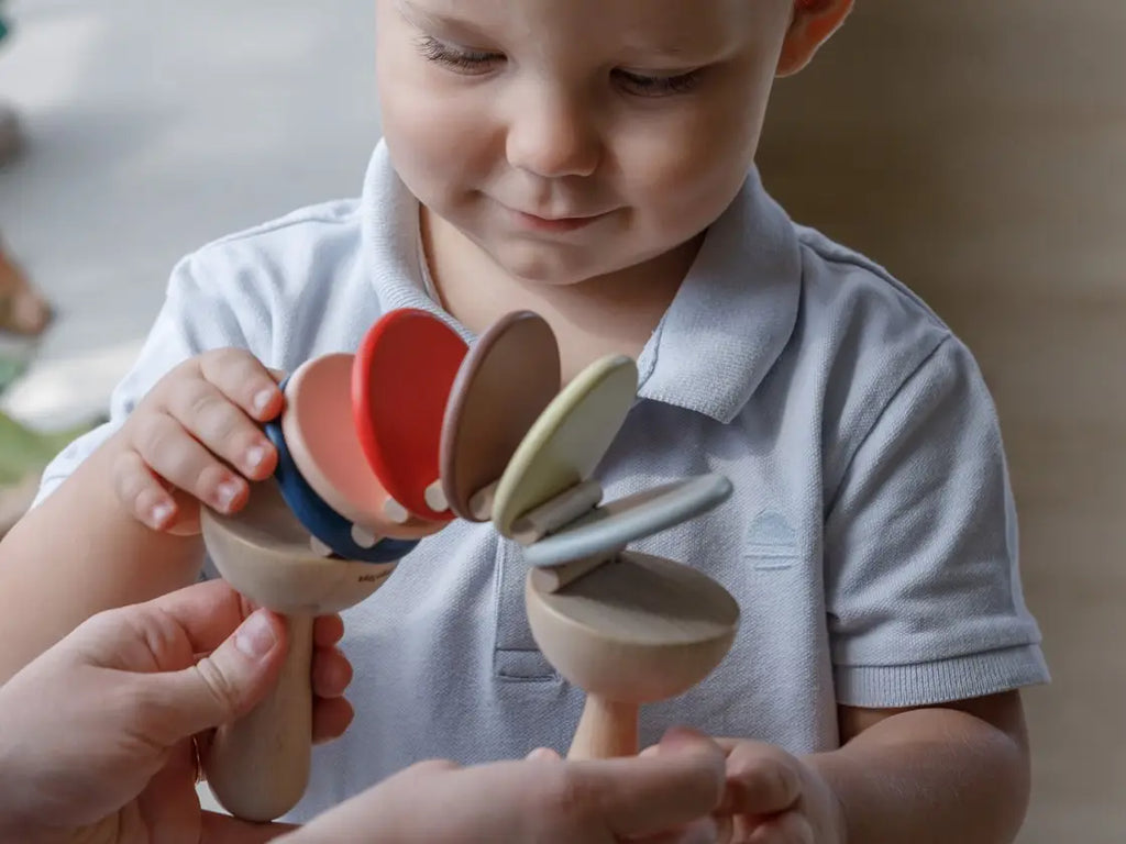 A young child with short hair examines two Clatter Percussion Toys held by an adult, depicting a moment of curiosity and learning with sustainably made toys.