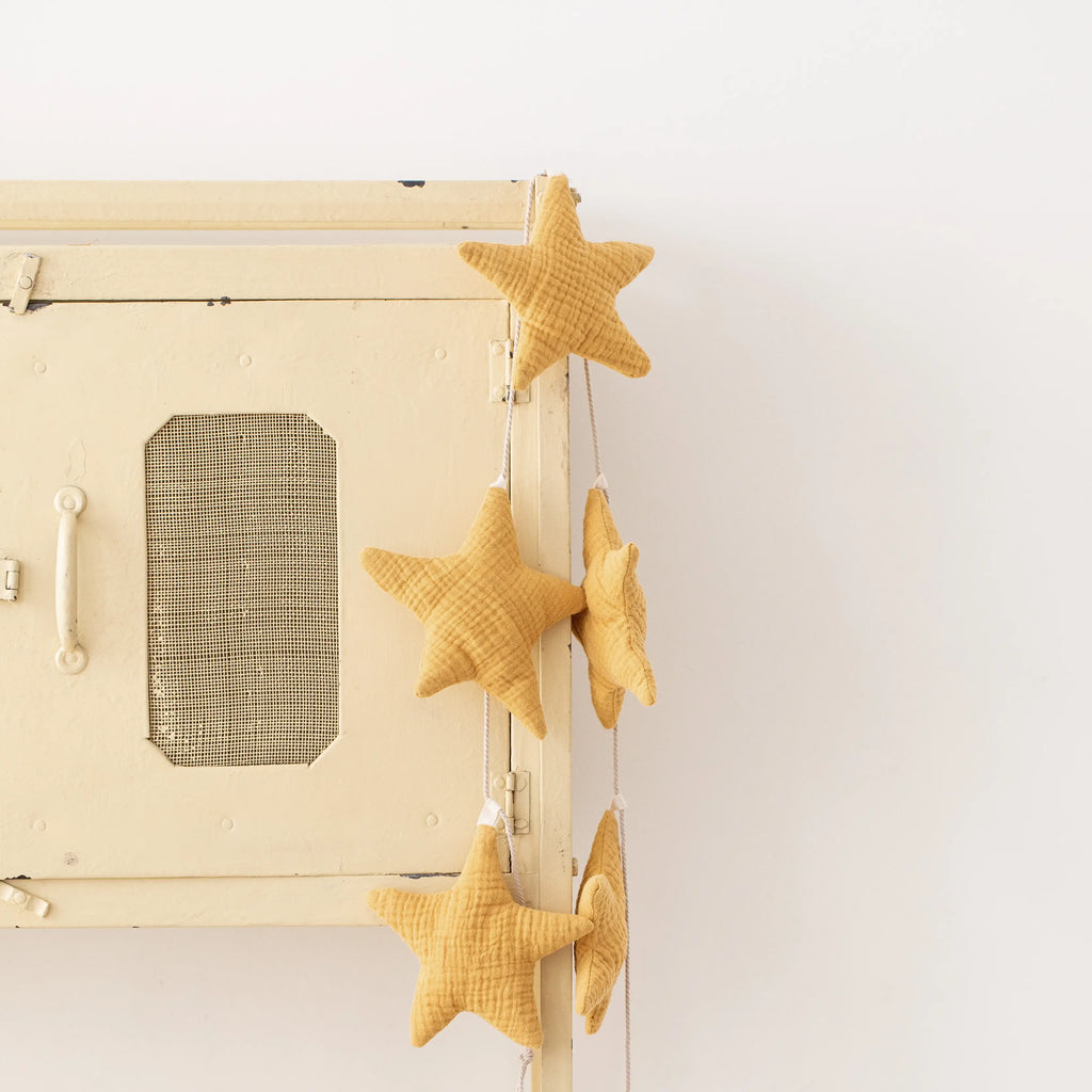 Vintage beige suitcase with Handmade Star Garland ornaments and neutral color garland hanging on a small white ladder against a plain background.