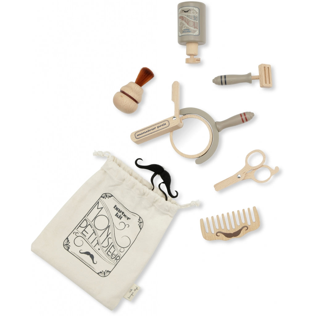 A collection of children's Pretend Play Wooden Barber Set beauty accessories, including a brush, mirror, lipstick, perfume bottle, scissors, hairdryer, and comb, all arranged neatly beside a drawstring bag.
