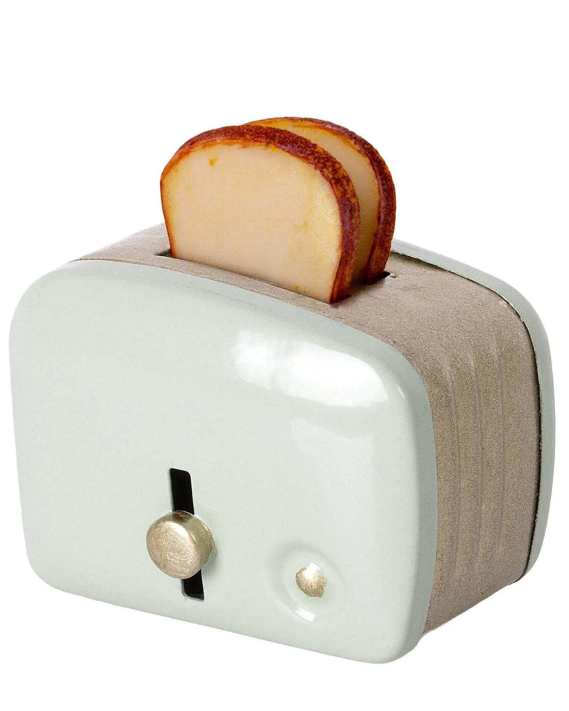 A slice of toasted bread shaped like an apple popping out of a Maileg | Miniature Toaster with a dial on the front. The toaster is set against a plain white background.