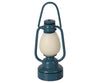 A Maileg Lantern with a white light bulb inside. This miniature lantern, designed with a classic, old-fashioned look, has a handle on top for easy carrying. It features non-rechargeable batteries that are easy to replace using the battery change tool included.