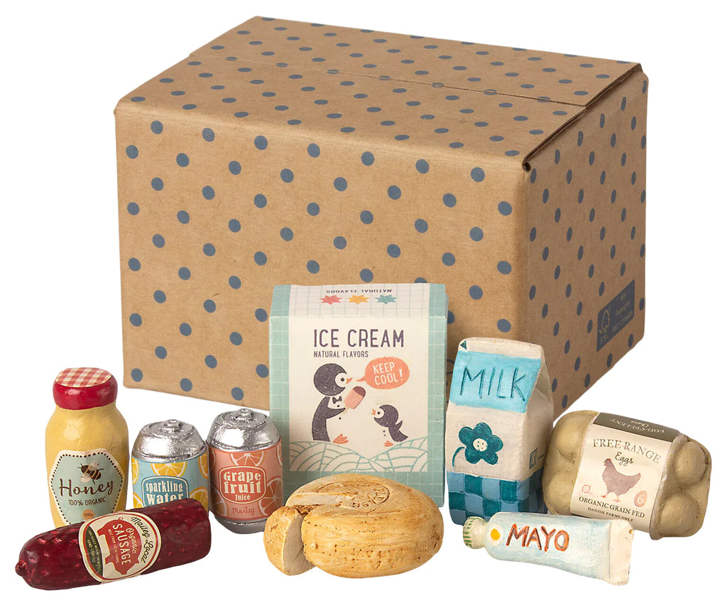 A collection of Maileg Miniature Grocery Box including honey, bread, canned goods, and drinks, displayed in front of a cardboard box with a vintage ice cream advertising poster.