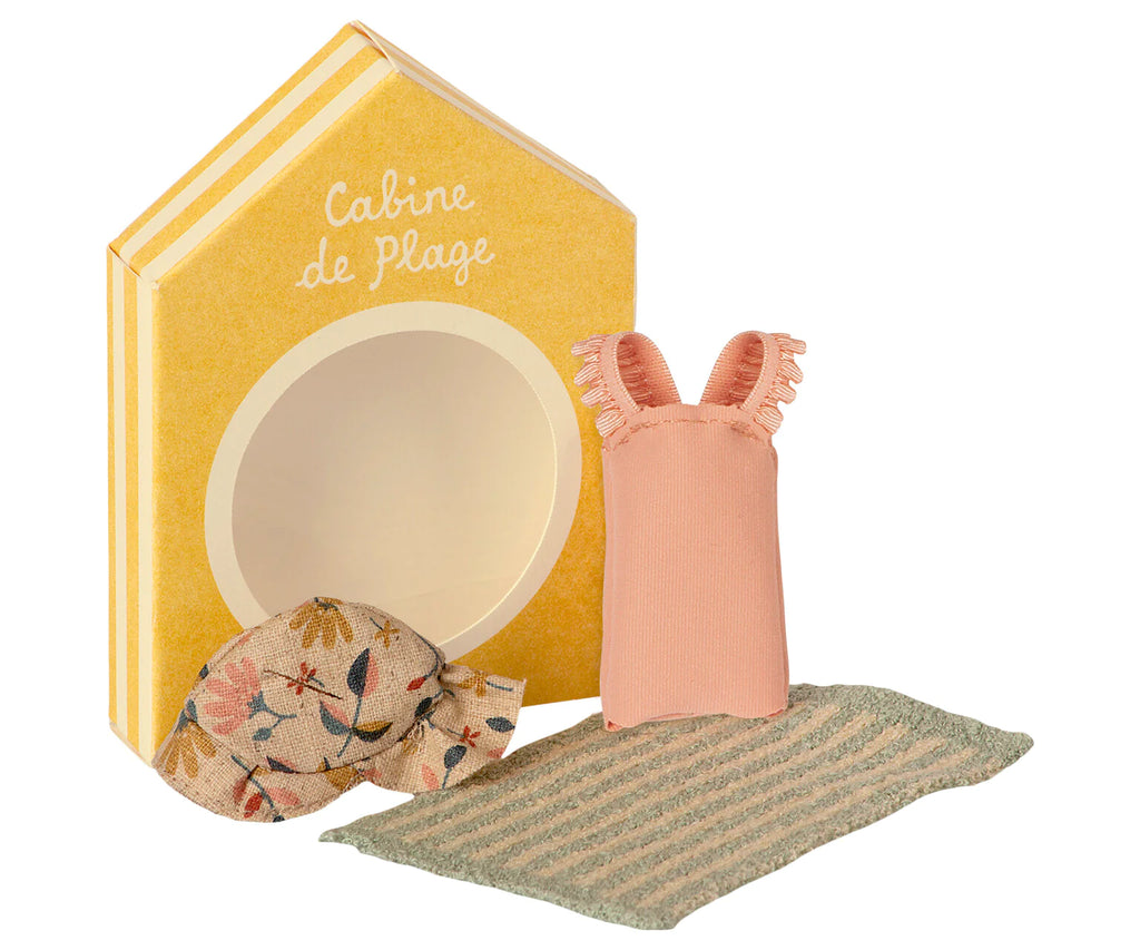 The Maileg Beach Set for Big Sister includes a yellow toy beach cabin box labeled "Cabine de Plage," a floral-patterned soft toy resembling a ball, a small striped green towel, and a pink dress with frilled sleeves—perfect beach accessories for big sister mice.