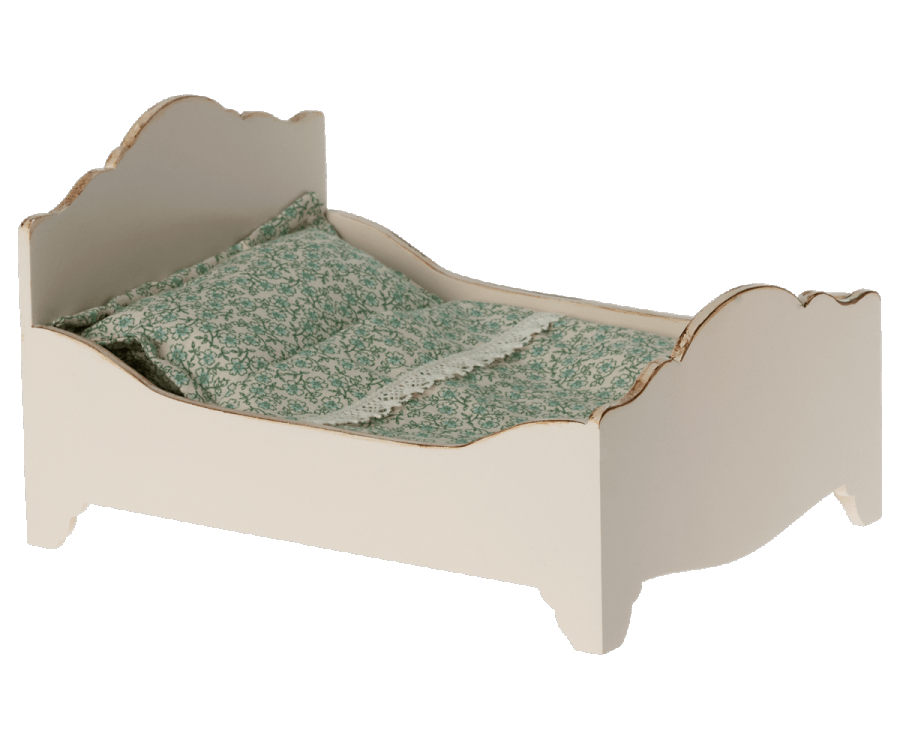 A quaint Maileg wooden bed painted in pastel cream, featuring elegantly curved edges and adorned with a green floral-printed bed linen.