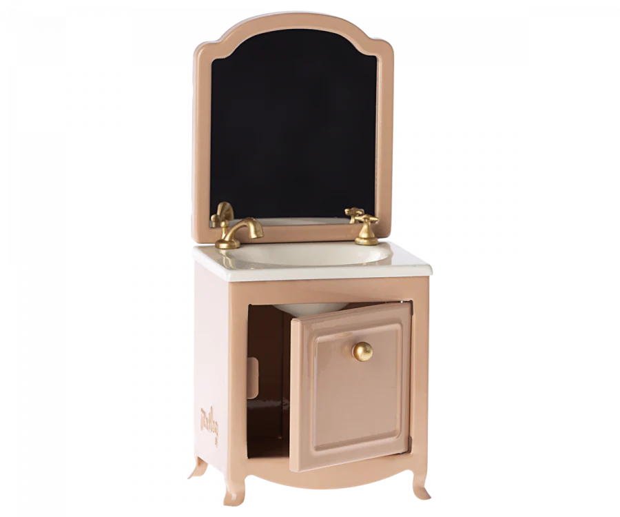 A child's Maileg Miniature Sink With Mirror in pastel pink with a removable gold-trimmed oval mirror, gold handles, a small drawer, and a cupboard.