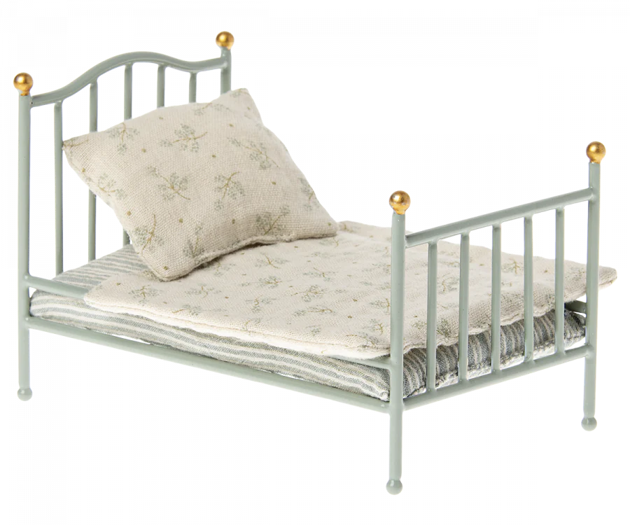 A Maileg Miniature Bed with a decorative headboard and footboard, holding a beige floral-patterned mattress and a matching pillow, isolated on a white background.