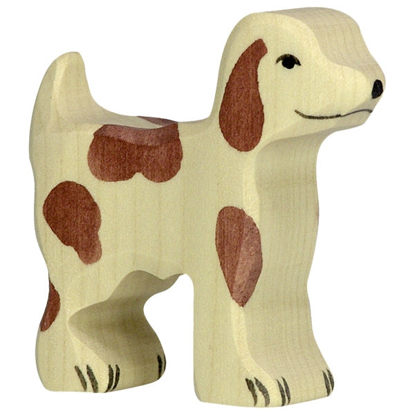 A Holztiger Small Farm Dog with a light beige body and brown spots. Made in Europe by HOLZTIGER figures, the dog has a simple, carved design with minimal features, including a smiling face with black eyes and nose, and a short, upright tail.