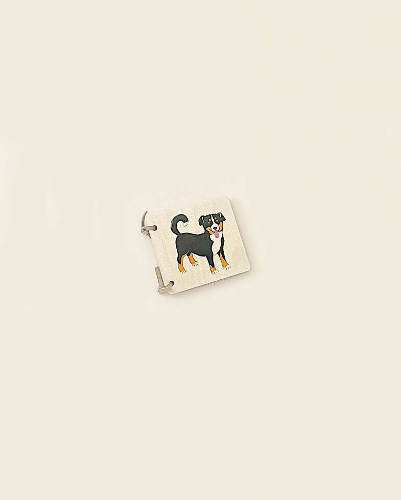A wooden picture book - animals featuring a painted enamel scene with a black and tan dog on a pastel yellow background, accented by a silver frame and clasp, Made in Switzerland.