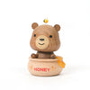 A Wooden Honey Bear Bobblehead figurine of a smiling bear sitting on a honey pot, with a small yellow bird perched on its head. The pot is labeled "honey" and has honey dripping.