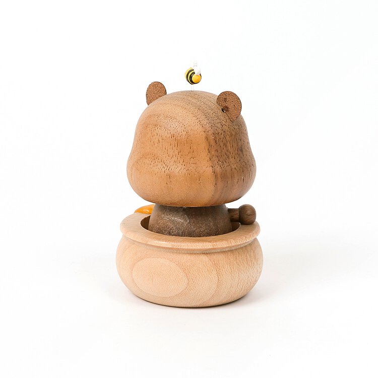 A wooden honey bear bobblehead with a small bell on its head, sitting on a rounded base, isolated on a white background.